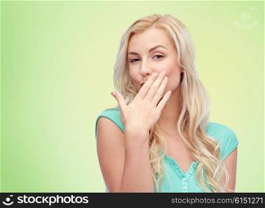 gesture and people concept - smiling young woman or teenage girl covering her mouth with hands over green natural background. smiling young woman or teen girl covering mouth