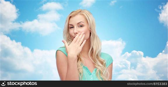gesture and people concept - smiling young woman or teenage girl covering her mouth with hands over blue sky and clouds background. smiling young woman or teen girl covering mouth