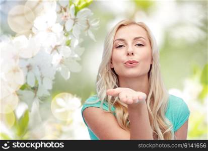 gesture and people concept - smiling young woman or teenage girl sending blow kiss over natural spring background. smiling young woman or teen girl sending blow kiss