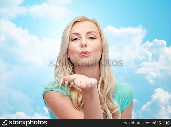 gesture and people concept - smiling young woman or teenage girl sending blow kiss over blue sky and clouds background. smiling young woman or teen girl sending blow kiss