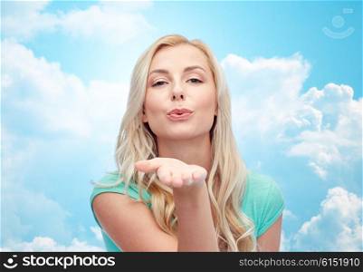 gesture and people concept - smiling young woman or teenage girl sending blow kiss over blue sky and clouds background. smiling young woman or teen girl sending blow kiss
