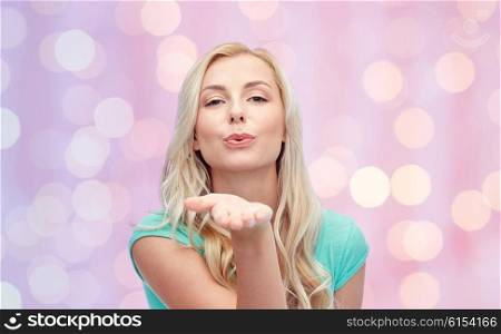 gesture and people concept - smiling young woman or teenage girl sending blow kiss over pink holidays lights background. smiling young woman or teen girl sending blow kiss