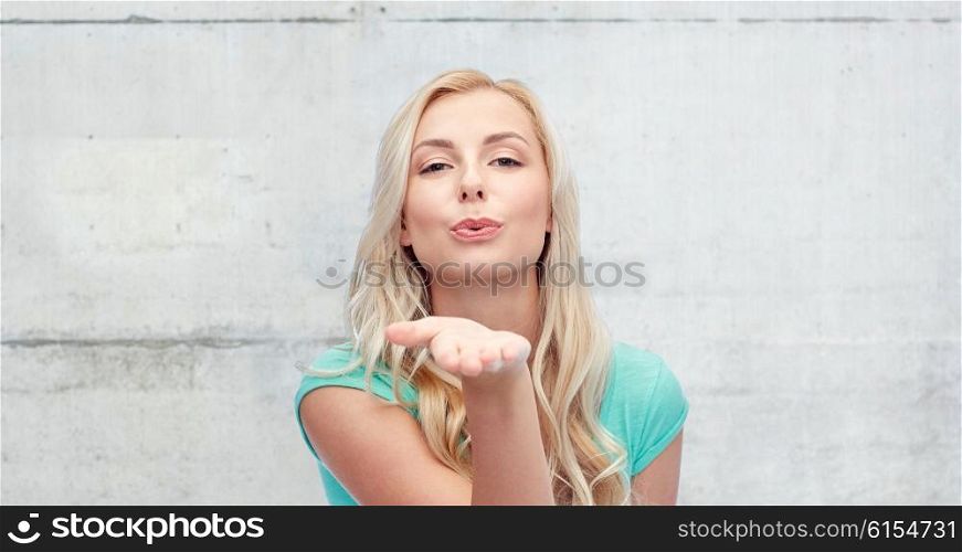 gesture and people concept - smiling young woman or teenage girl sending blow kiss over gray concrete wall background. smiling young woman or teen girl sending blow kiss