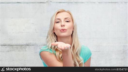 gesture and people concept - smiling young woman or teenage girl sending blow kiss over gray concrete wall background. smiling young woman or teen girl sending blow kiss