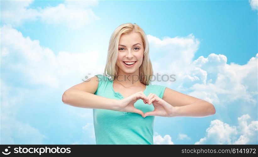 gesture and people concept - smiling young woman or teenage girl showing heart shape made of fingers over blue sky and clouds background. happy woman or teen girl showing heart shape sigh