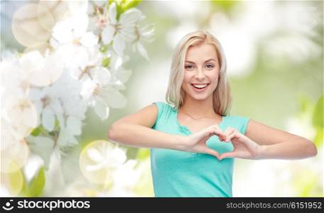 gesture and people concept - smiling young woman or teenage girl showing heart shape made of fingers over natural spring background. happy woman or teen girl showing heart shape sigh