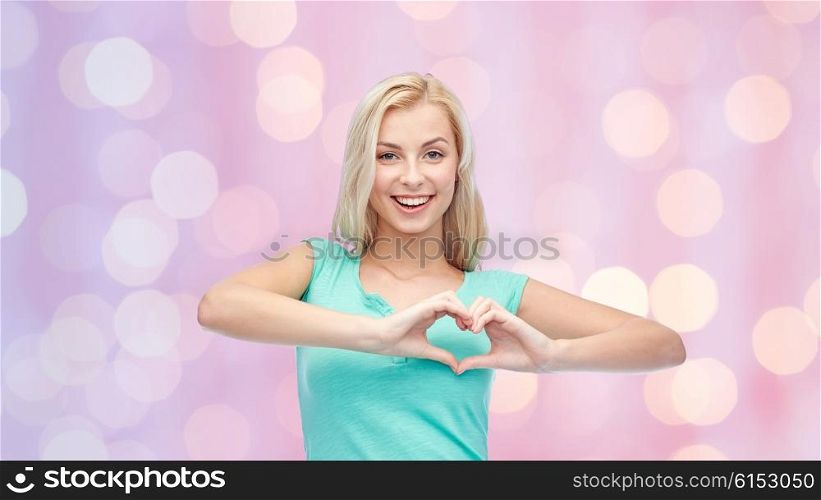 gesture and people concept - smiling young woman or teenage girl showing heart shape made of fingers over pink holidays lights background. happy woman or teen girl showing heart shape sigh