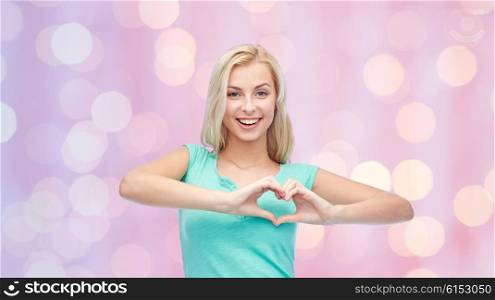 gesture and people concept - smiling young woman or teenage girl showing heart shape made of fingers over pink holidays lights background. happy woman or teen girl showing heart shape sigh