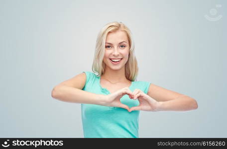 gesture and people concept - smiling young woman or teenage girl showing heart shape made of fingers over gray background. happy woman or teen girl showing heart shape sigh