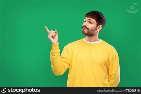 gesture and people concept - young man in yellow sweatshirt pointing finger to something over emerald green background. man pointing finger to something over green