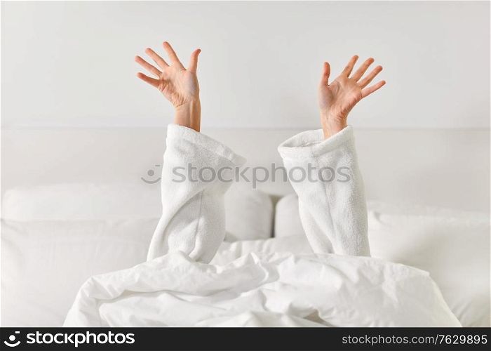 gesture, comfort and morning concept - hands of young woman in hotel robe lying in bed and stretching at bedroom. hands of woman lying in bed and stretching