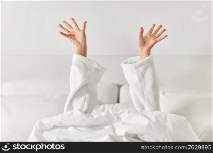 gesture, comfort and morning concept - hands of young woman in hotel robe lying in bed and stretching at bedroom. hands of woman lying in bed and stretching