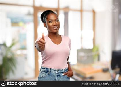 gesture, corporate and people concept - smiling young african american woman showing thumbs up over office background. african woman showing thumbs up at office