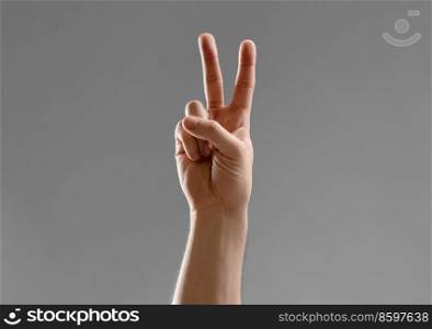 gesture, count and people concept - close up of male hand showing peace over grey background. close up of male hand showing peace gesture