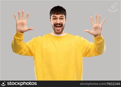 gesture, count and people concept - happy smiling young man in yellow sweatshirt showing his hand or ten fingers over grey background. smiling young man showing his hand or ten fingers