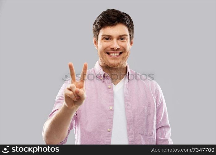 gesture, count and people concept - smiling young man showing two fingers or peace hand sign over grey background. young man showing two fingers or peace hand sign