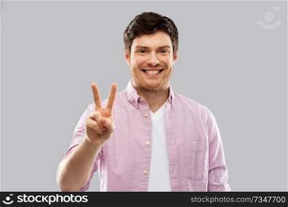 gesture, count and people concept - smiling young man showing two fingers or peace hand sign over grey background. young man showing two fingers or peace hand sign