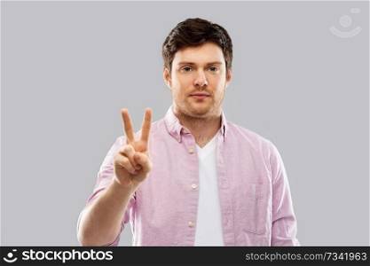 gesture, count and people concept - young man showing two fingers or peace hand sign over grey background. young man showing two fingers over grey background