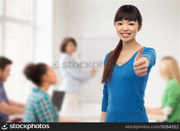 gesture, education and people concept - happy smiling young asian student woman showing thumbs up over school classroom background. happy smiling young woman showing thumbs up. happy smiling young woman showing thumbs up