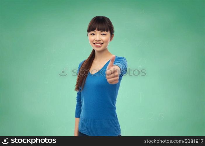 gesture, education and people concept - happy smiling young asian woman showing thumbs up over green school chalkboard background. happy smiling young woman showing thumbs up