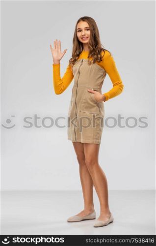 gesture, emotion and people concept - happy smiling young teenage girl in mustard yellow top waving hand over grey background. happy smiling young teenage girl waving hand