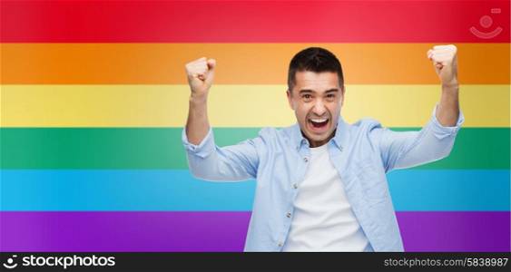 gesture, emotions, homophobia and people concept - angry gay man with raised hands over rainbow flag stripes background