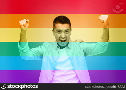 gesture, emotions, homophobia and people concept - angry gay man with raised hands over rainbow flag stripes background