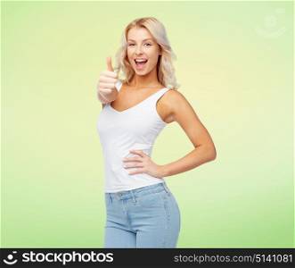 gesture, expressions and people concept - happy smiling young woman in white top and jeans showing thumbs up over green background. happy young woman showing thumbs up