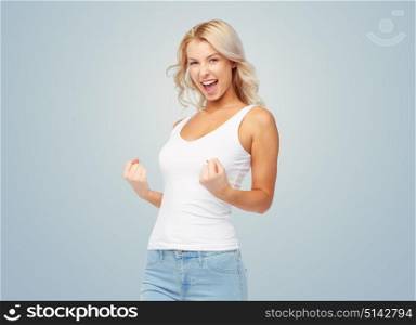 gesture, expressions and people concept - happy smiling young woman in white top and jeans doing fist pump over blue background. happy young woman doing fist pump gesture