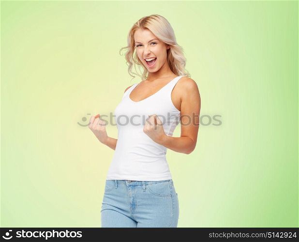 gesture, expressions and people concept - happy smiling young woman in white top and jeans doing fist pump over green background. happy young woman doing fist pump gesture