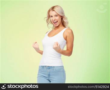 gesture, expressions and people concept - happy smiling young woman in white top and jeans doing fist pump over green background. happy young woman doing fist pump gesture