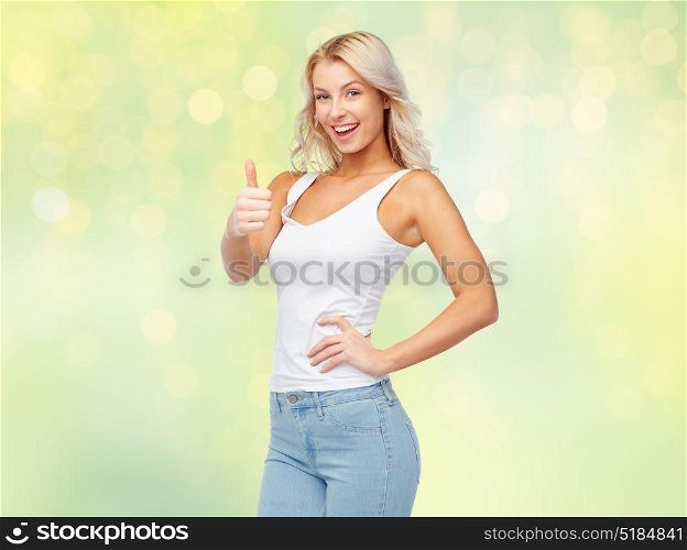 gesture, expressions and people concept - happy smiling young woman in white top and jeans showing thumbs up over summer green lights background. happy young woman showing thumbs up