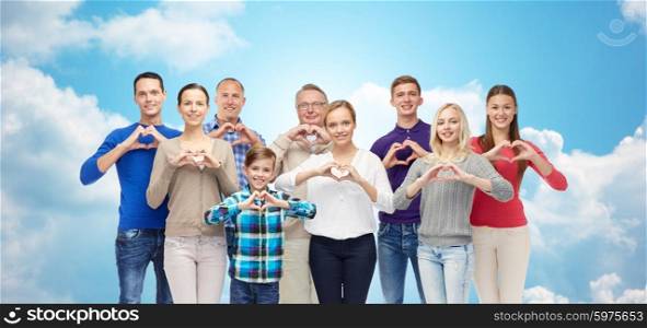 gesture, family, generation and people concept - group of smiling men, women and boy showing heart shape hand sign over blue sky and clouds background