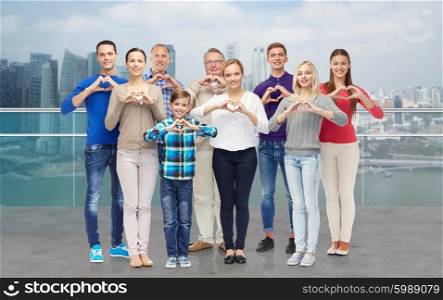 gesture, family, generation and people concept - group of smiling men, women and boy showing heart shape hand sign over singapore city waterside background