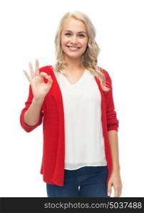 gesture, fashion, portrait and people concept - happy smiling young woman in red cardigan showing ok hand sign over white. happy smiling young woman showing ok hand sign