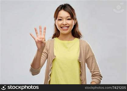 gesture, finger counting and people concept - smiling asian woman showing four fingers over grey background. smiling asian woman showing four fingers