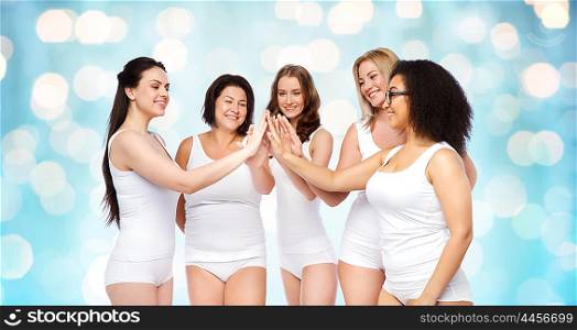 gesture, friendship, beauty, body positive and people concept - group of happy different women in white underwear making high five over blue holidays lights background