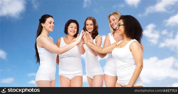 gesture, friendship, beauty, body positive and people concept - group of happy different women in white underwear making high five over blue sky and clouds background