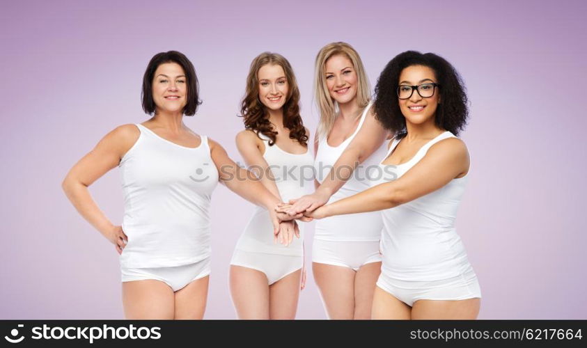 gesture, friendship, beauty, body positive and people concept - group of happy different women in white underwear holding hands together on top over violet background