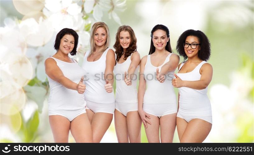 gesture, friendship, beauty, body positive and people concept - group of happy different women in white underwear showing thumbs up over natural spring cherry blossom background