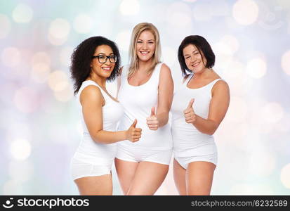 gesture, friendship, beauty, body positive and people concept - group of happy plus size women in white underwear showing thumbs up over holidays lights background