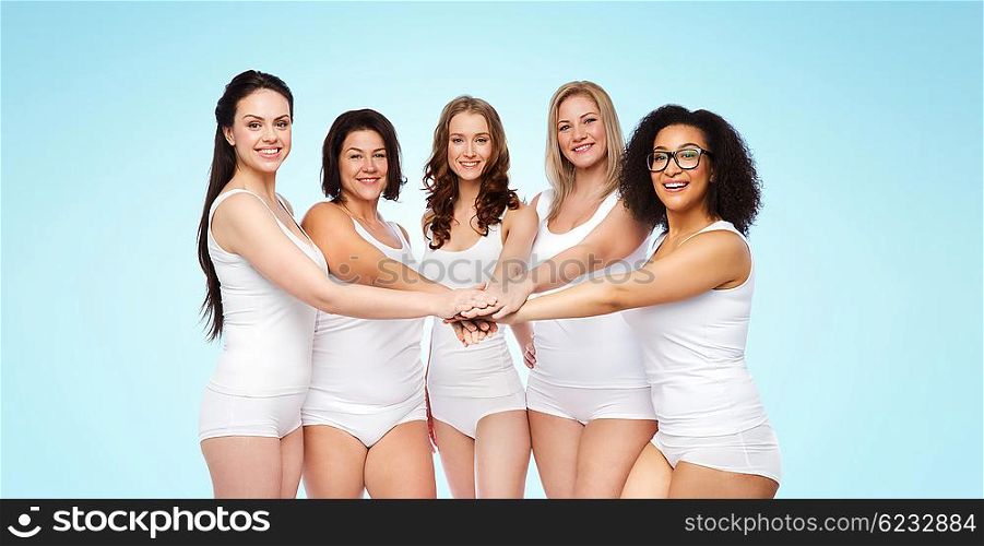 gesture, friendship, beauty, body positive and people concept - group of happy different women in white underwear holding hands together on top over blue background