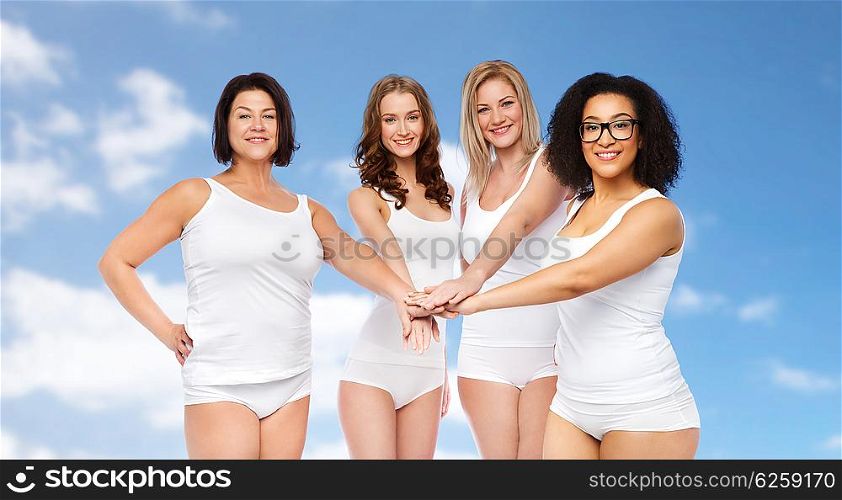 gesture, friendship, beauty, body positive and people concept - group of happy different women in white underwear holding hands together on top over blue sky and clouds background