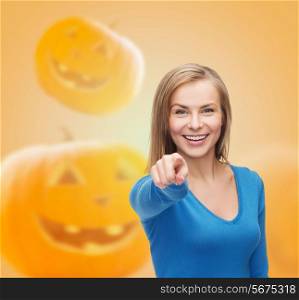 gesture, holidays and people concept - smiling young woman pointing finger at you over pumpkins background