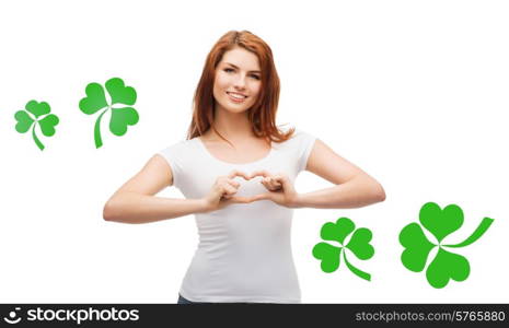 gesture, holidays, st. patricks day and happy people concept - smiling girl in white blank t-shirts showing heart with hands over white background with green shamrock or clover