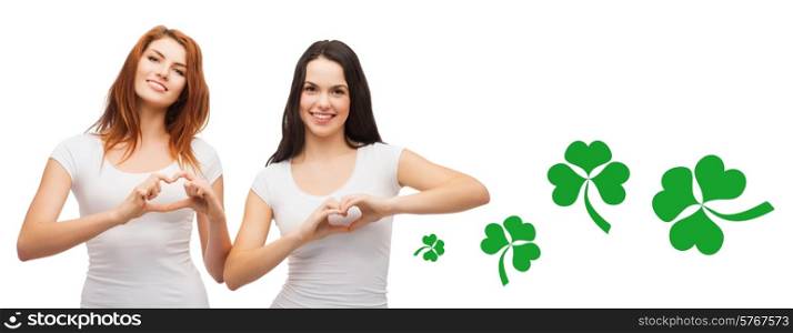 gesture, holidays, st. patricks day and happy people concept - smiling girls in white blank t-shirts showing heart with hands over white background with green shamrock or clover