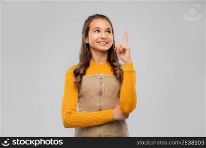 gesture, idea and people concept - happy smiling young teenage girl pointing finger up over grey background. smiling young teenage girl pointing finger up