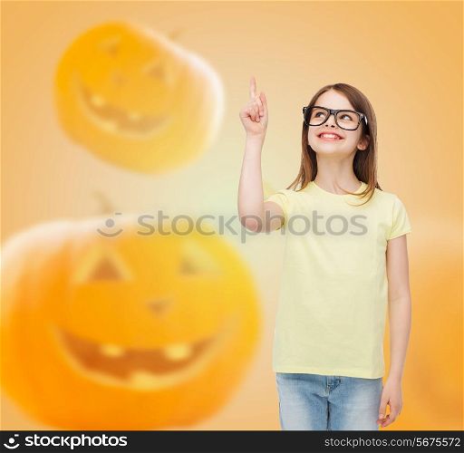 gesture, idea, education, holidays and people concept - smiling little girl in glasses pointing finger over halloween pumpkins background