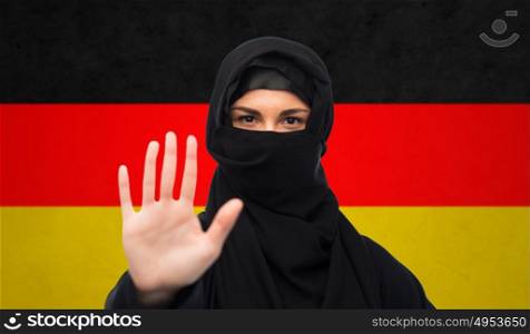 gesture, immigration, religious prohibition and people concept - muslim woman in hijab showing stop sign over german flag background. muslim woman in hijab showing stop sign