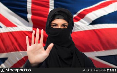 gesture, immigration, religious prohibition and people concept - muslim woman in hijab showing stop sign over british flag background. muslim woman in hijab showing stop sign